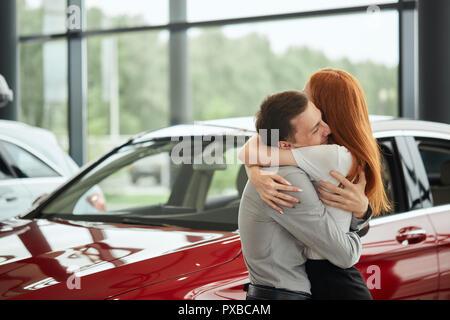 Giovane donna felice sorpresa da una nuova macchina a car showroom, dono da suo marito Foto Stock