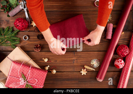 Mani femminili decorare dono le caselle rosse per vacanze di Natale e Capodanno. Le mani vicino. Presente il confezionamento di idee. Foto Stock