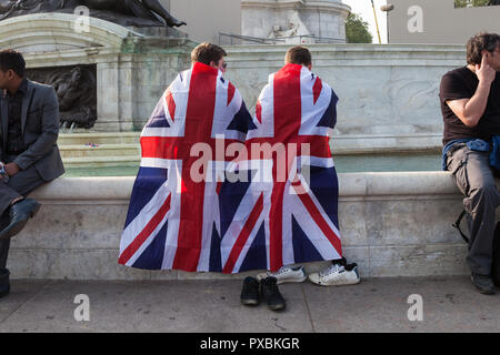 Due giovani uomini avvolti in Unione Jack flag e il raffreddamento i loro piedi nella fontana fuori Buckingham Palace. Foto Stock