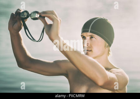 Nuotatore modello in un mare guardando attraverso googles al tramonto Foto Stock