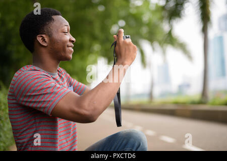 Bel giovane uomo africano di scattare foto con la fotocamera in posizione di parcheggio Foto Stock