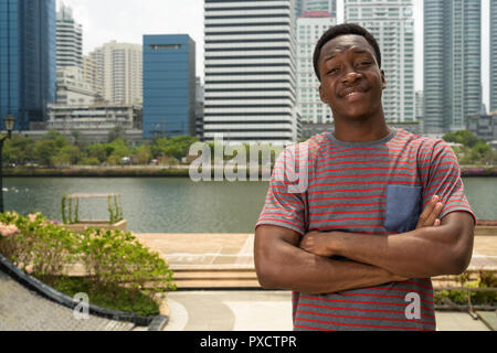 Felice giovane bello uomo africano con le braccia incrociate in città Foto Stock