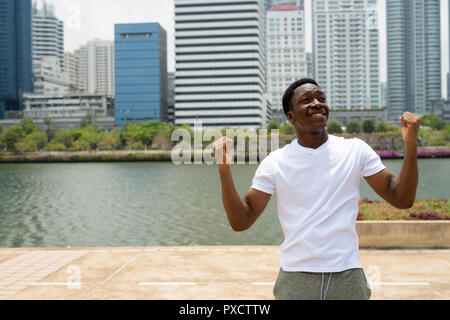 Bel giovane uomo africano con le braccia sollevate all'aperto con il paesaggio sullo sfondo Foto Stock