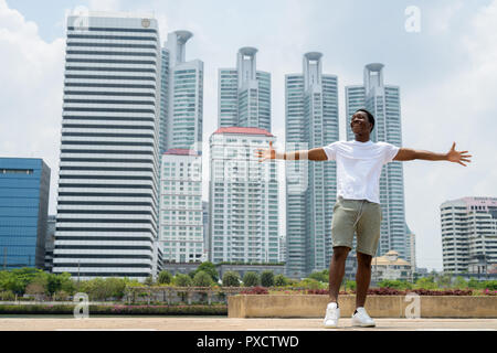 Bel giovane uomo africano con le braccia sollevate all'aperto con il paesaggio sullo sfondo Foto Stock