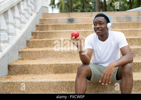 L'uomo africano ascolto di musica con cuffie e azienda red apple Foto Stock