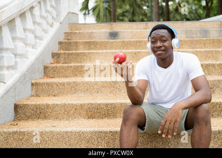 L'uomo africano ascolto di musica con cuffie e azienda red apple Foto Stock