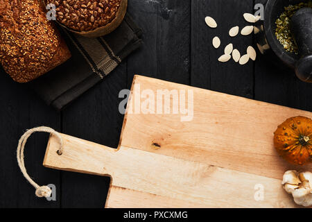 Tagliere e vari crostini di pane integrale, aglio, semi di zucca e di mortaio su tavoli in legno nero. Vista da sopra con copia spazio per testo, menu o Foto Stock