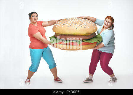 Divertente immagine di divertenti, chubby donne su sfondo bianco. Due donne sono in possesso di un enorme panino Foto Stock