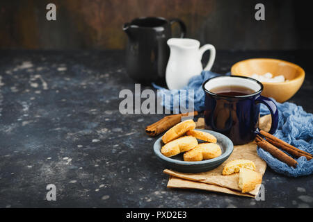 Smaltato blu tazza di tè, bastoncini di cannella, anice stelle e pasta frolla su uno sfondo scuro. Spazio per il testo. Foto Stock