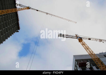 Costruzione di un moderno ed alto monolitico edificio rinforzato e gru di colore giallo con un cielo blu in background, vista dal basso Foto Stock