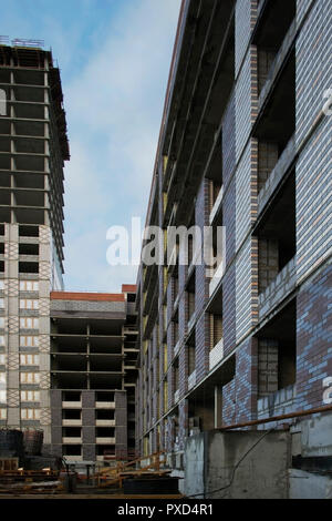 Costruzione di un alto e moderno edificio residenziale monolitico di cemento armato e mattoni sullo sfondo di pulire il cielo blu, pareti, windows un Foto Stock