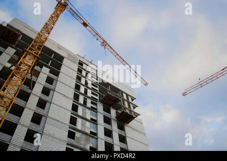 Costruzione di un moderno ed alto monolitico edificio rinforzato e gru di colore giallo con un cielo blu in background, vista dal basso Foto Stock