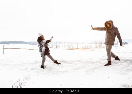 Carefree felice coppia giovane divertirsi insieme nella neve in inverno bosco tirare palle di neve a ogni altro durante la simulazione di una lotta. Foto Stock