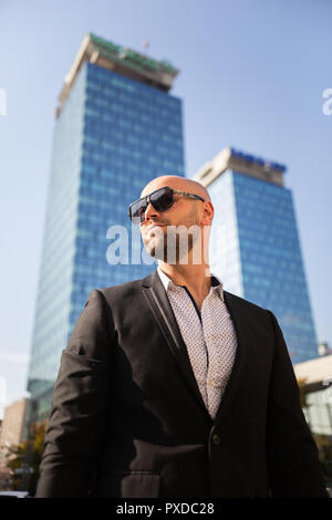 Bello ed elegante imprenditore con occhiali da sole di fronte all edificio per uffici Foto Stock