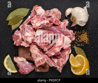 Crudo fresco di capra spezzatino di carne come tagli su nero tagliere con spezie (semi di senape, aglio, limone e foglie di alloro). Foto Stock