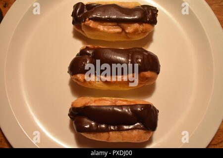 Un delizioso Trio di cioccolato francese Eclair pasticcini serviti su una piastra bianca Foto Stock