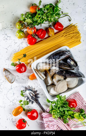 Gli ingredienti per cucinare gli spaghetti con frutti di mare. Gusci musselsa, vongole, vongole, pomodori e vino bianco. Foto Stock