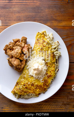 Cibo venezuelano. Il mais CACHAPA con il formaggio e il maiale fritto - cochino frito. Sfondo di legno, vista dall'alto Foto Stock