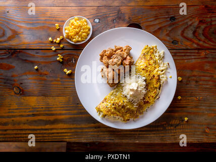 Cibo venezuelano. Il mais CACHAPA con il formaggio e il maiale fritto - cochino frito. Sfondo di legno, vista dall'alto Foto Stock