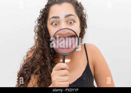 La donna che mostra la sua linguetta ingrandita attraverso una lente di ingrandimento Foto Stock