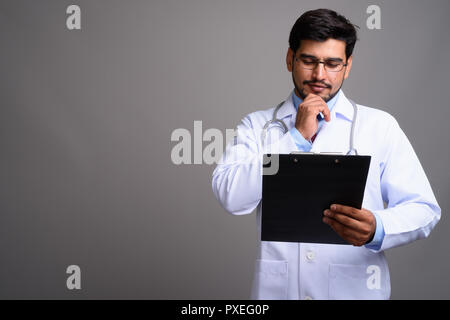 Giovane bello barbuto uomo persiano medico contro backgroun grigio Foto Stock