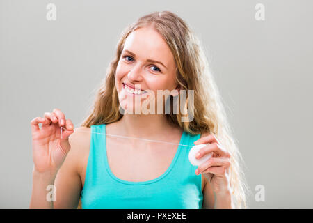 Bella giovane donna usando il filo interdentale su sfondo grigio. Foto Stock