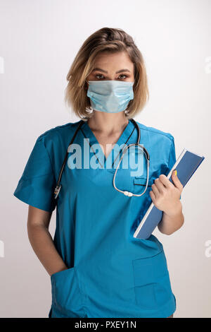 Ritratto di giovane medico con stetoscopio indossando maschera facciale azienda i risultati della carta e in piedi dritto. Professionali di medico specialista Foto Stock