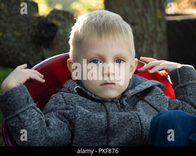 Piccolo Ragazzo caucasico seduto in poltrona in giardino Foto Stock