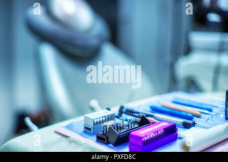 Messa a fuoco selettiva delle necessarie apparecchiature odontoiatriche e strumento di lavoro per il dentista sedia in background e sfocati ufficio medico. a freddo e toni di blu Foto Stock