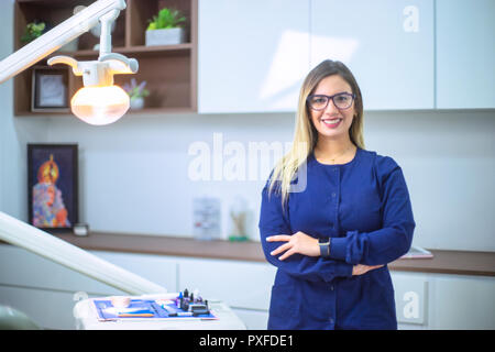 Ritratto di donna dentista sorridente in ufficio dentale vestita di azzurro uniforme medica Foto Stock