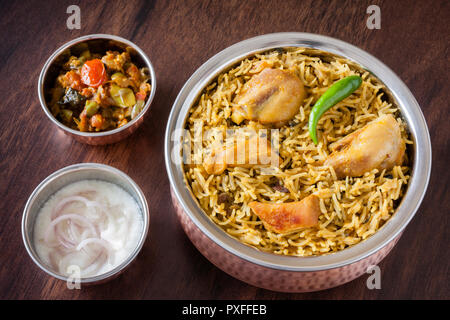 Primo piano vista dalla cima di delizie indiane biryani di pollo servito in autentici utensili in rame con lati tradizionali, raita e sugo di carne. Foto Stock