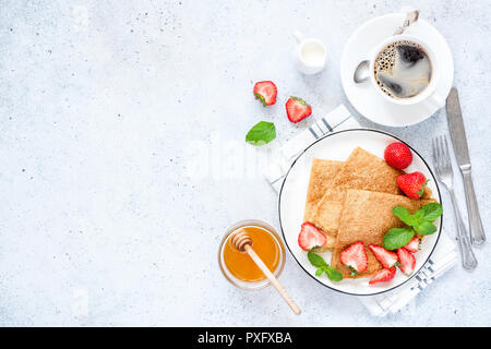 Crepes francese o russo Blini con fragole fresche, il miele, il caffè sul cemento dello sfondo. Una sana colazione gustosa. Tabella vista superiore, spazio di copia Foto Stock