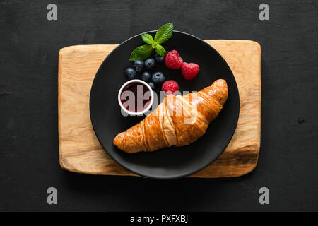 Croissant con frutti di bosco e confettura sulla piastra nera, tabella vista dall'alto. Foto Stock