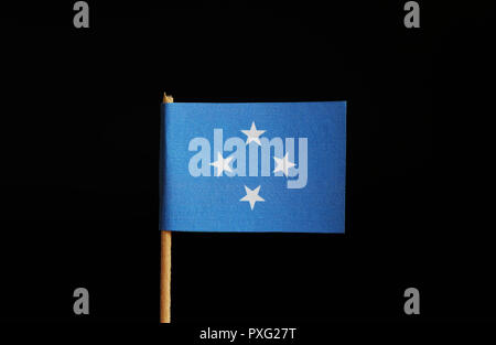 Una bandiera nazionale degli Stati Federati di Micronesia sulla bacchetta di legno su sfondo nero. La federazione appartiene a Oceania. Gruppo di isole. Foto Stock