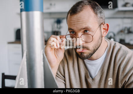 Ritratto di ingegnere belli guardando al di sopra di bicchieri al modello di razzo a casa Foto Stock