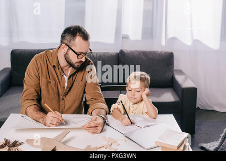 Padre e figlio piccolo disegno mentre la modellazione di piano assieme a casa Foto Stock