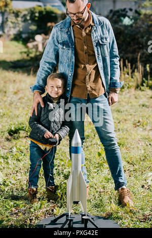 Padre felice con il piccolo figlio di sorridere alla telecamera mentre giocando con il modello rocket outdoor Foto Stock