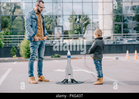 Padre guardando il piccolo figlio di lancio di razzi modello per esterno Foto Stock