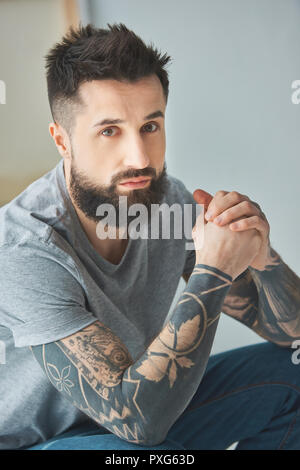 Ritratto di uomo barbuto con tatuaggi guardando la fotocamera Foto Stock
