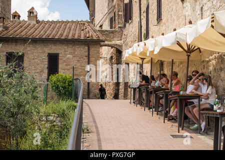 Persone con bevande al cafe' sul marciapiede in ombra, nella cittadina collinare di San Gimignano, Toscana, Italia Foto Stock