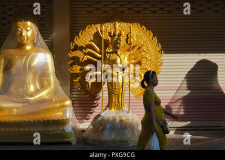 Una donna su un inizio di mattina, oltrepassando statue buddiste poste al di fuori di un negozio per gli artefatti buddista, Bamrung Muang Rd., Bangkok, Thailandia Foto Stock