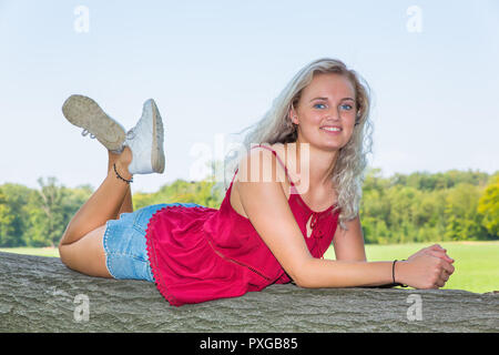 Giovane donna caucasica giacente sul tronco di albero in natura Foto Stock