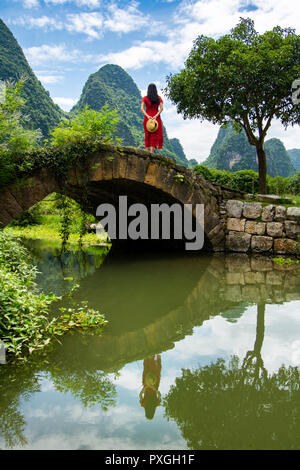 Ragazza in abito rosso stand in un antico ponte in pietra di Yangshuo Foto Stock