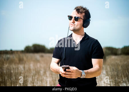 Bel giovane la riproduzione di brani musicali dal proprio smartphone su le sue cuffie Foto Stock