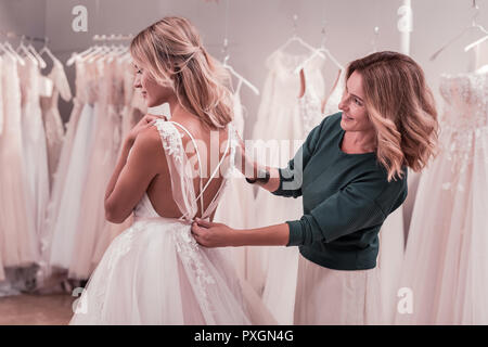 Piacevole donna felice aiutando a sua figlia di indossare l'abito Foto Stock