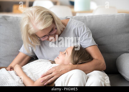 Carino bambina rilassarsi sulle ginocchia della nonna in un momento di relax a casa Foto Stock