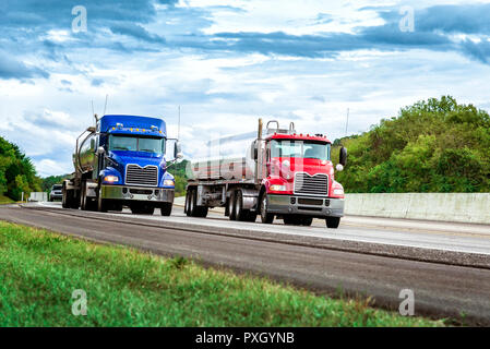 Inquadratura orizzontale di due benzina autocisterne sulla Interstate. Uno ha una cabina rosso e l'altra una cabina blu. Cielo nuvoloso. Foto Stock