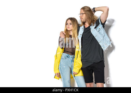 Attraente giovane uomo in abiti eleganti abbracciando la sua ragazza in maglietta trasparente ed impermeabile giallo su bianco Foto Stock