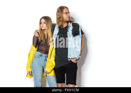 Bel giovane in abiti eleganti abbracciando la sua ragazza in maglietta trasparente ed impermeabile giallo su bianco Foto Stock