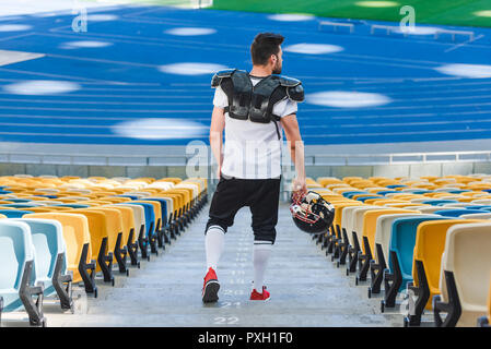 Vista posteriore del giovane giocatore di football americano su scale presso lo stadio sportivo Foto Stock